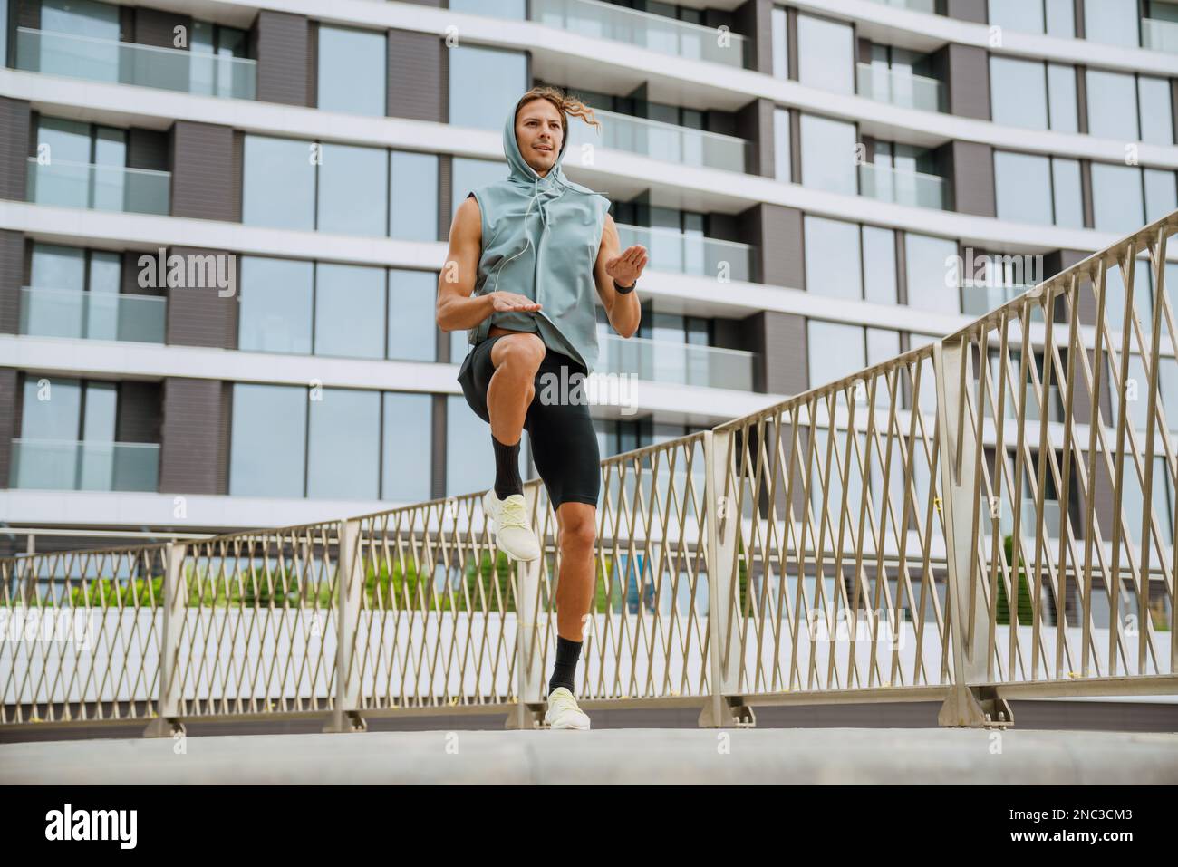 Giovane atletico uomo bello dai capelli lunghi che fa esercizi fisici, mentre si trova vicino a un edificio moderno all'aperto Foto Stock