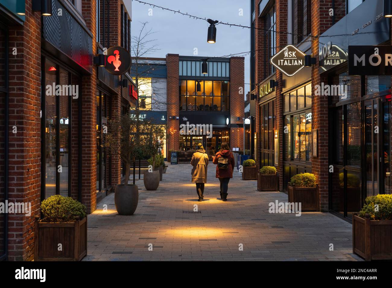 Persone illuminate dai riflettori e camminando attraverso il centro commerciale Bell Court al crepuscolo a Stratford Upon Avon, Inghilterra Foto Stock