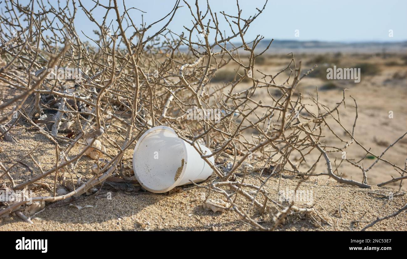 Rifiuti di tazza di plastica su una duna di sabbia, fuoco selettivo. Foto Stock