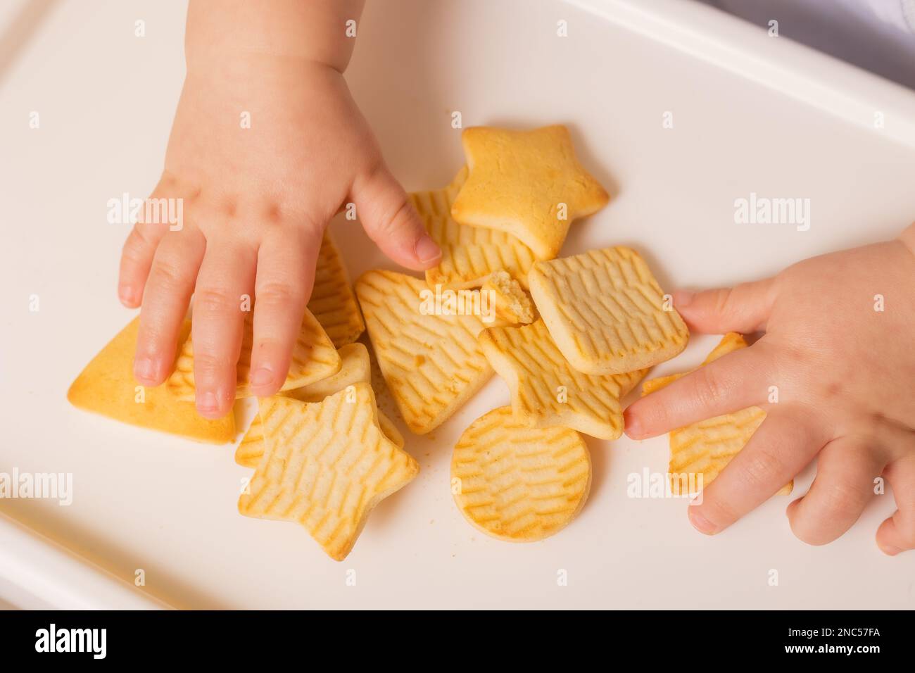 un bambino cute sta sedendosi nella sedia del bambino che mangia i biscotti. Sfondo giallo. Pappe per bambini, spazio per il testo. Foto di alta qualità Foto Stock