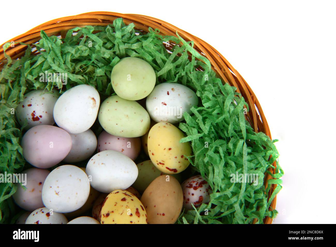 Mini uova di Pasqua al cioccolato in paglia verde su un cestino di vimini su sfondo bianco Foto Stock