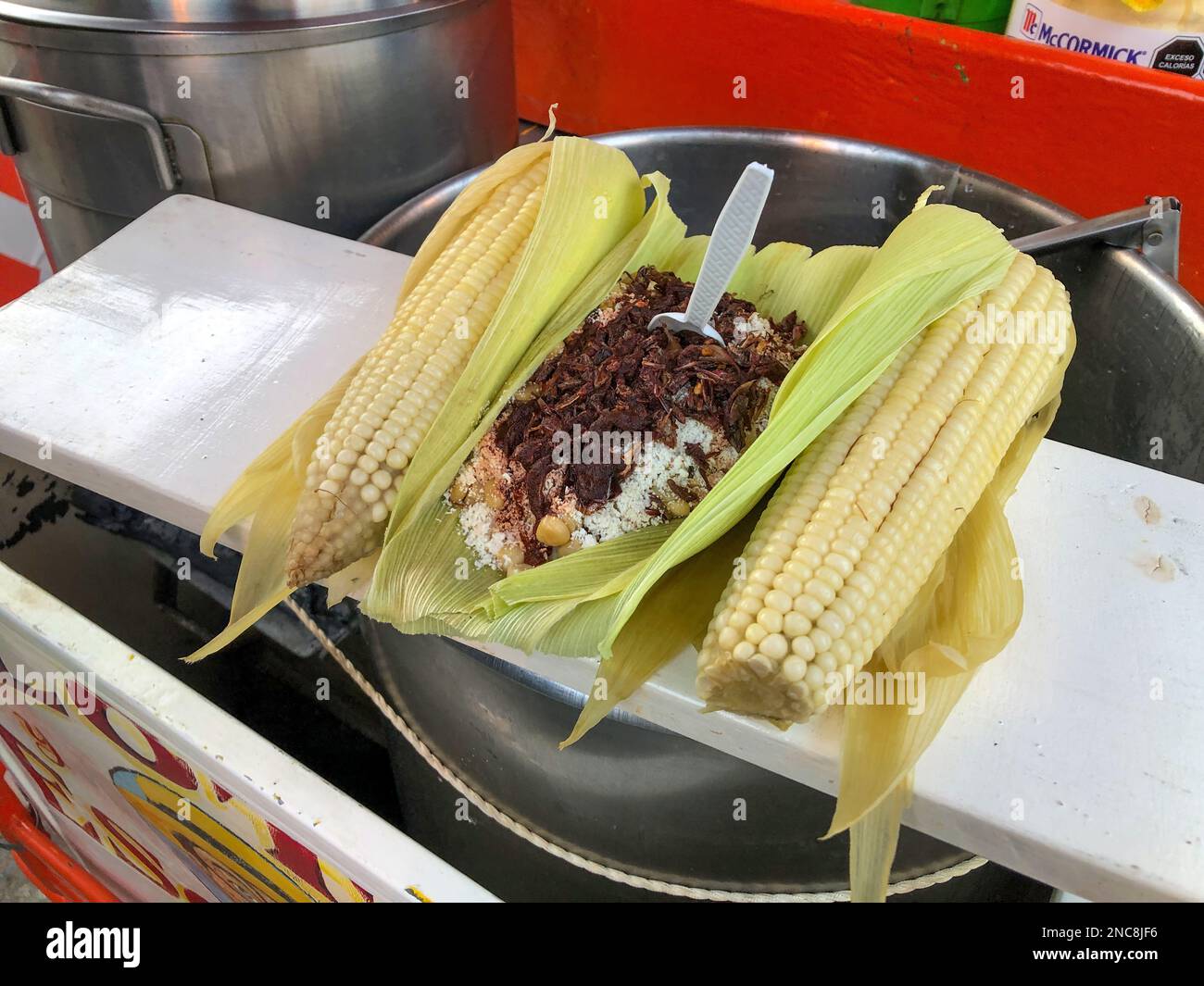 Esquites, un cibo di strada tradizionale messicano, un carrello di strada a Oaxaca, Messico, guarnito con cappuline o cavallette arrostite. Foto Stock