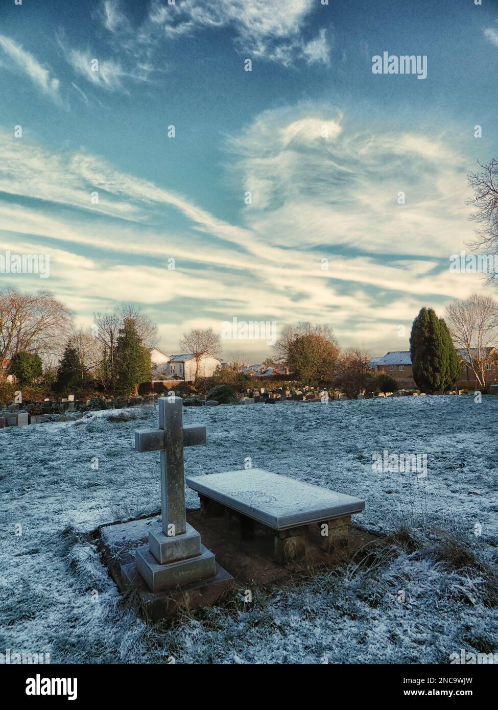 un cimitero e una croce di pietra in una fredda mattina d'inverno con brina a terra, cielo azzurro e sole. Foto Stock