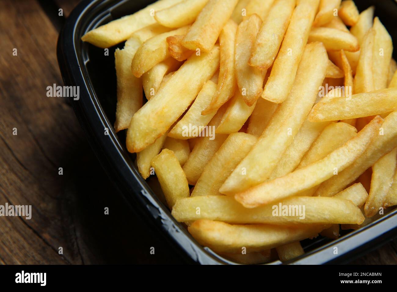 Contenitore con patatine fritte su tavolo di legno, primo piano. Servizio di consegna cibo Foto Stock