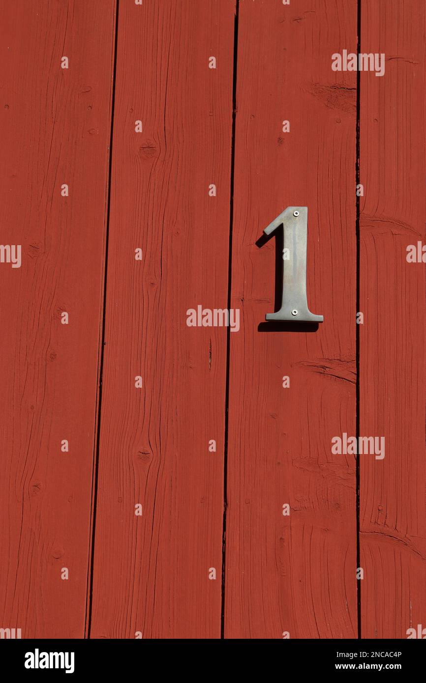 cartello bianco numero uno su una porta rossa con strisce orizzontali, numero civico Foto Stock