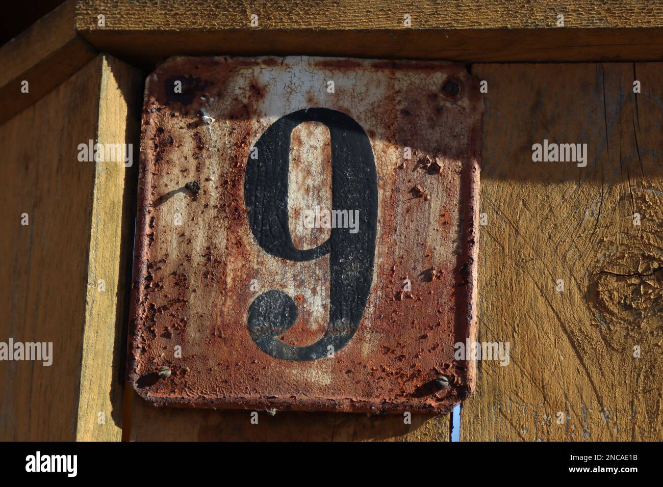 casa numero 9 recinzione di legno giallo con un segno di indirizzo di metallo, vecchio rustico marrone sfondo stagionato, nero numero nove cifra Foto Stock