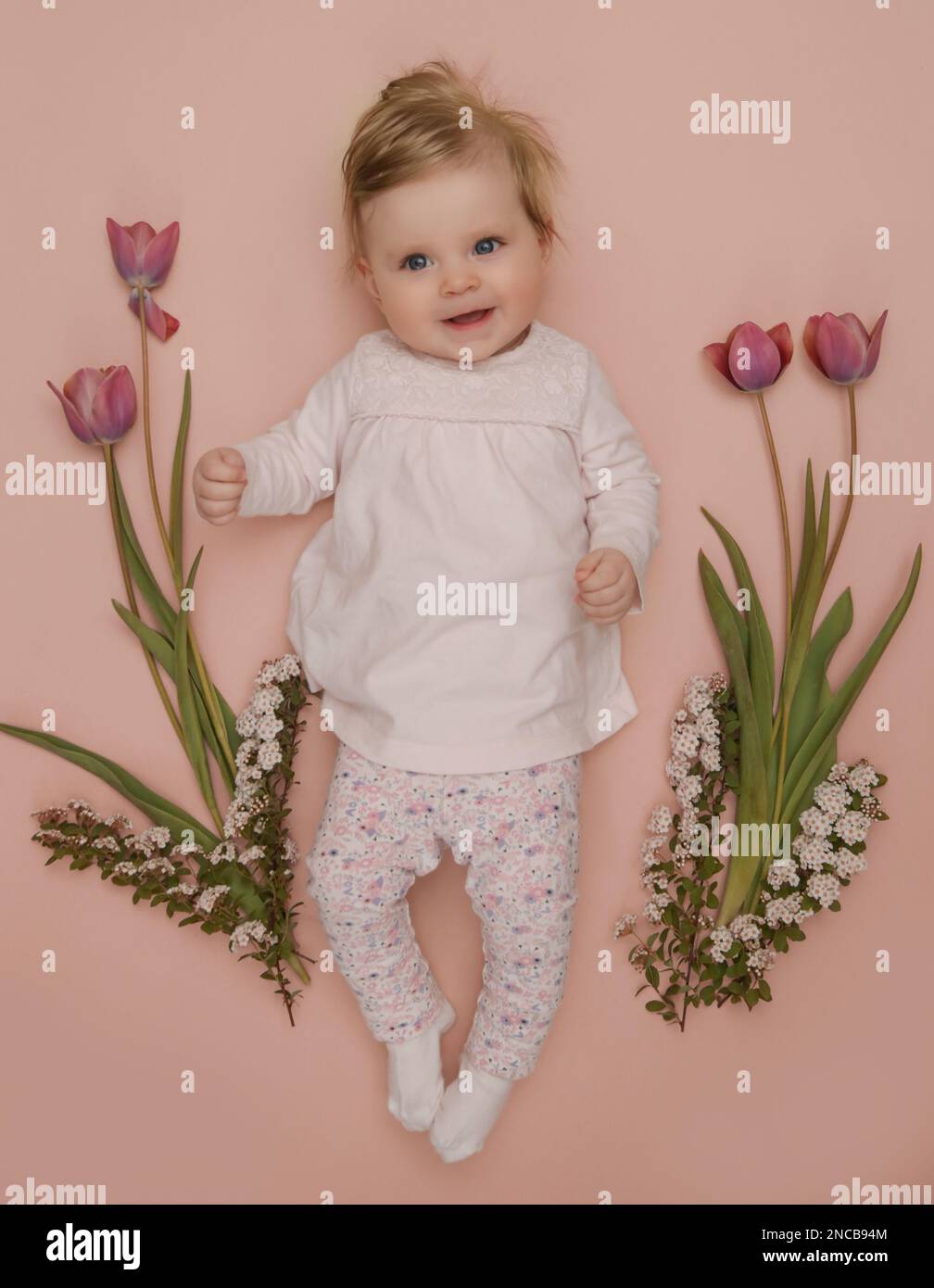 Adorabile bambino di cinque mesi con tulipani rosa primaverili. Herald di primavera. Sessione cardine per neonati e neonati. Composizione primaverile. Fotografia di neonati Foto Stock