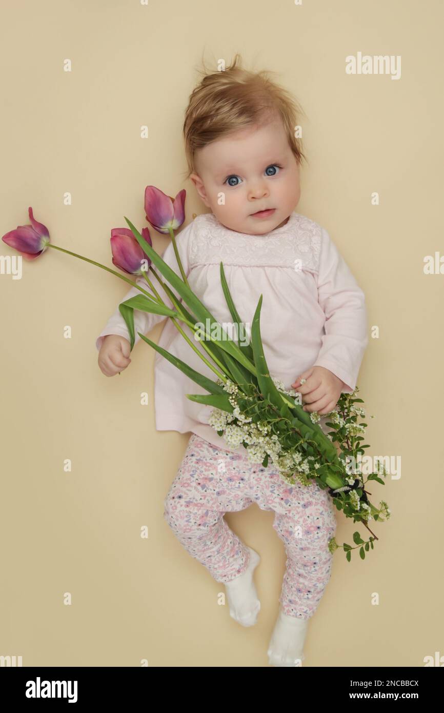 Adorabile bambino di cinque mesi con tulipani rosa primaverili. Herald di primavera. Sessione cardine per neonati e neonati. Composizione primaverile. Fotografia di neonati Foto Stock