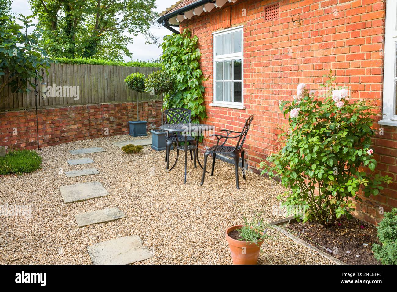 UK giardino patio design. Terreno duro con pietre di York passo in pietra in ghiaia e un tavolo da bistrot in metallo e sedie. Foto Stock