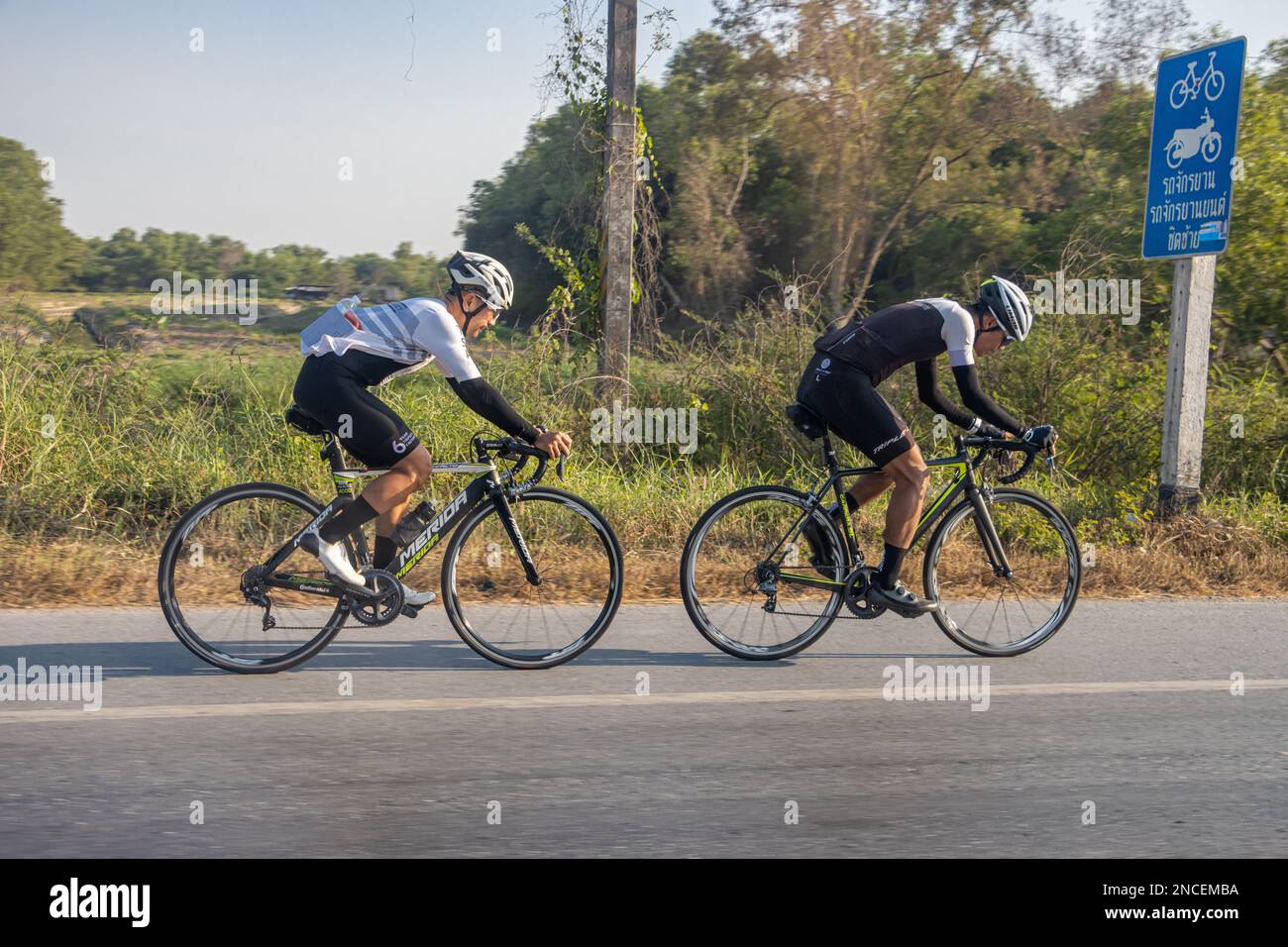 Un paio di ciclisti sta guidando su una strada con una pista ciclabile marcata, Thailandia Foto Stock