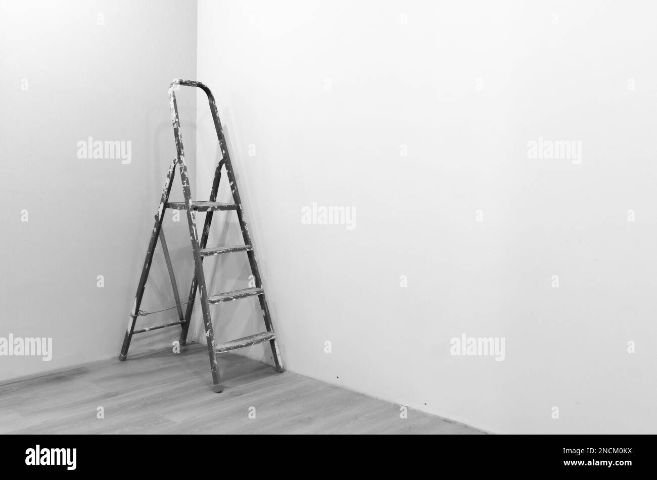 Fotografia in bianco e nero di una scala per riparare una vernice bianca macchiata in piedi nell'angolo di una stanza appena dipinta sul nuovo piano. Foto Stock