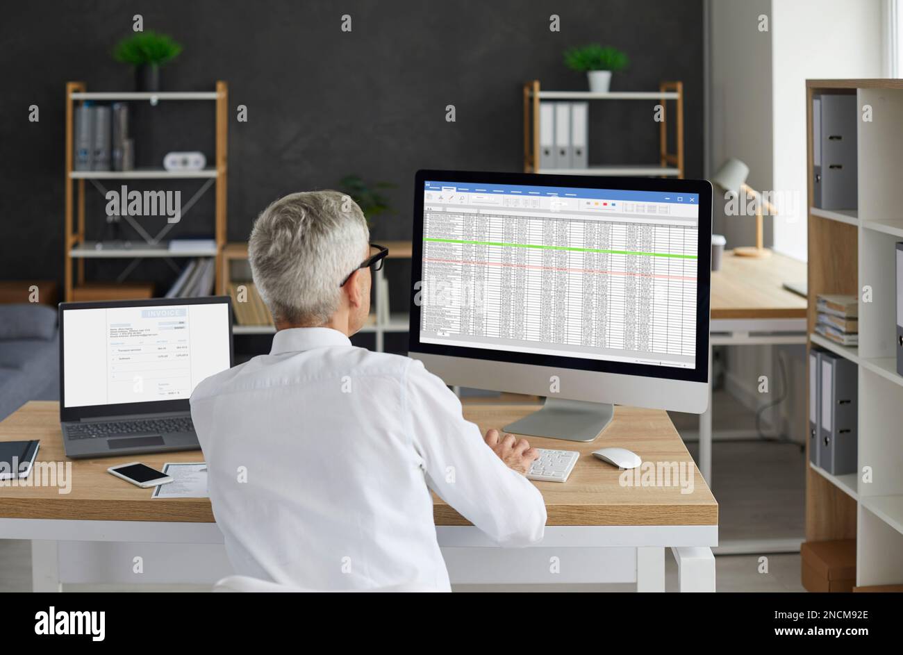Contabile maschile senior che lavora in ufficio e utilizza fogli di calcolo aziendali sul computer Foto Stock