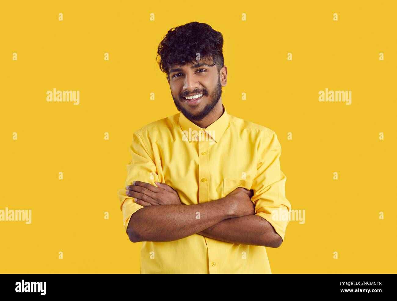 Giovane uomo indiano di etnia in elegante camicia sorridente in posa larga con le braccia incrociate sul petto Foto Stock