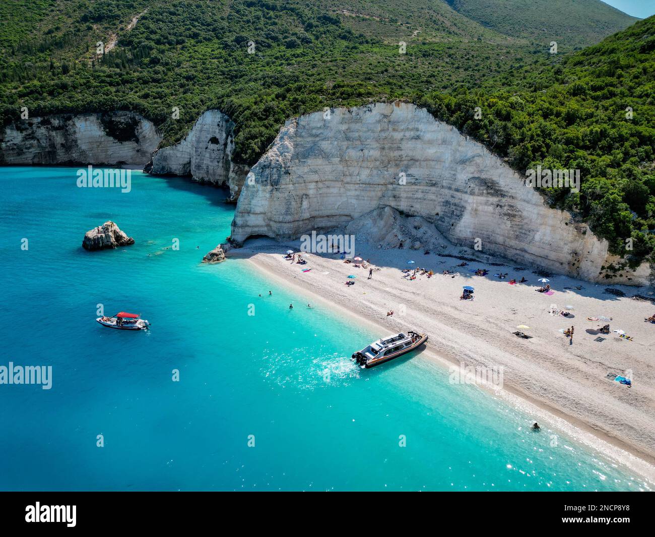 4K lontano fuco di Fteri Beach, Cefalonia, Cefalonia, Grecia con la collina calcarea, taxi in barca e la gente prendere il sole Foto Stock