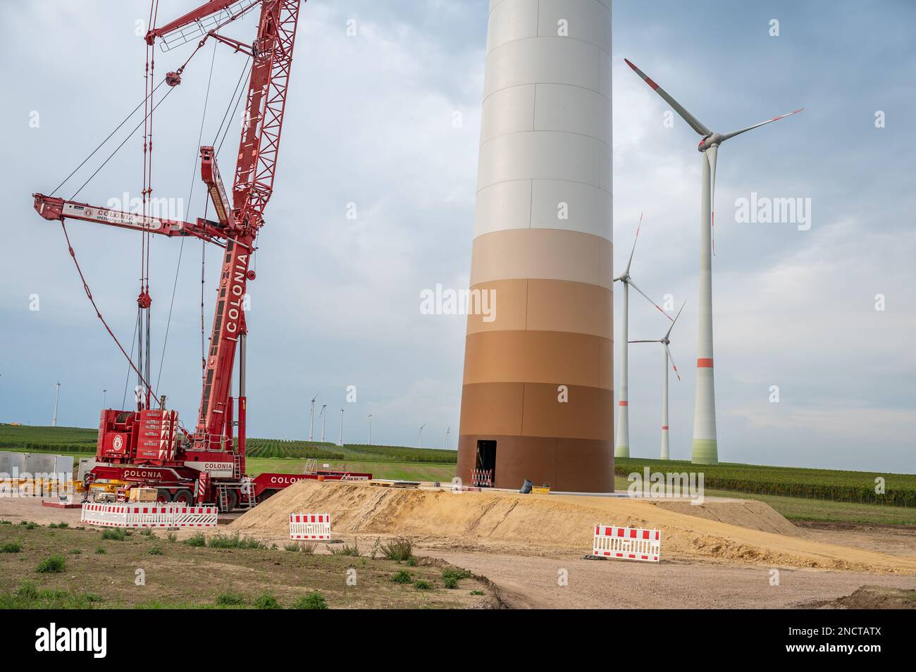 Cantiere di una turbina eolica, gru accanto alla torre della turbina eolica, turbine eoliche completate in background, vista ad angolo basso, giorno nuvoloso Foto Stock