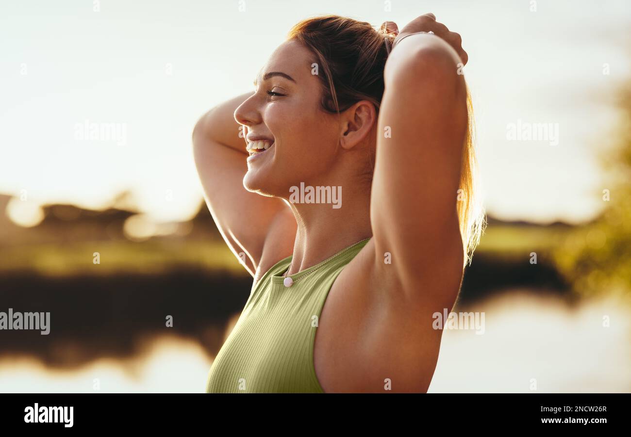 Donna Yoga legando i capelli mentre si trova accanto ad un lago. Donna felice che si prepara per un allenamento mattutino all'aperto. Donna che pratica uno stile di vita sano. Foto Stock