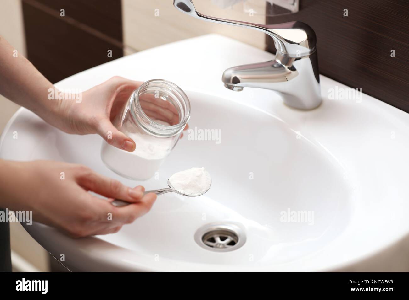 Donna che usa bicarbonato di sodio per disintasare lo scarico del lavandino in bagno, primo piano Foto Stock