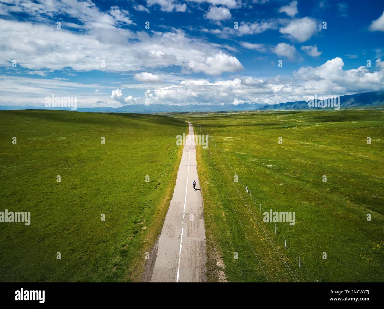L'uomo in mountain bike corre sulla strada asfaltata sulla valle di montagna contro il cielo nuvoloso blu. Concetto di svago e stile di vita sano. Foto Stock