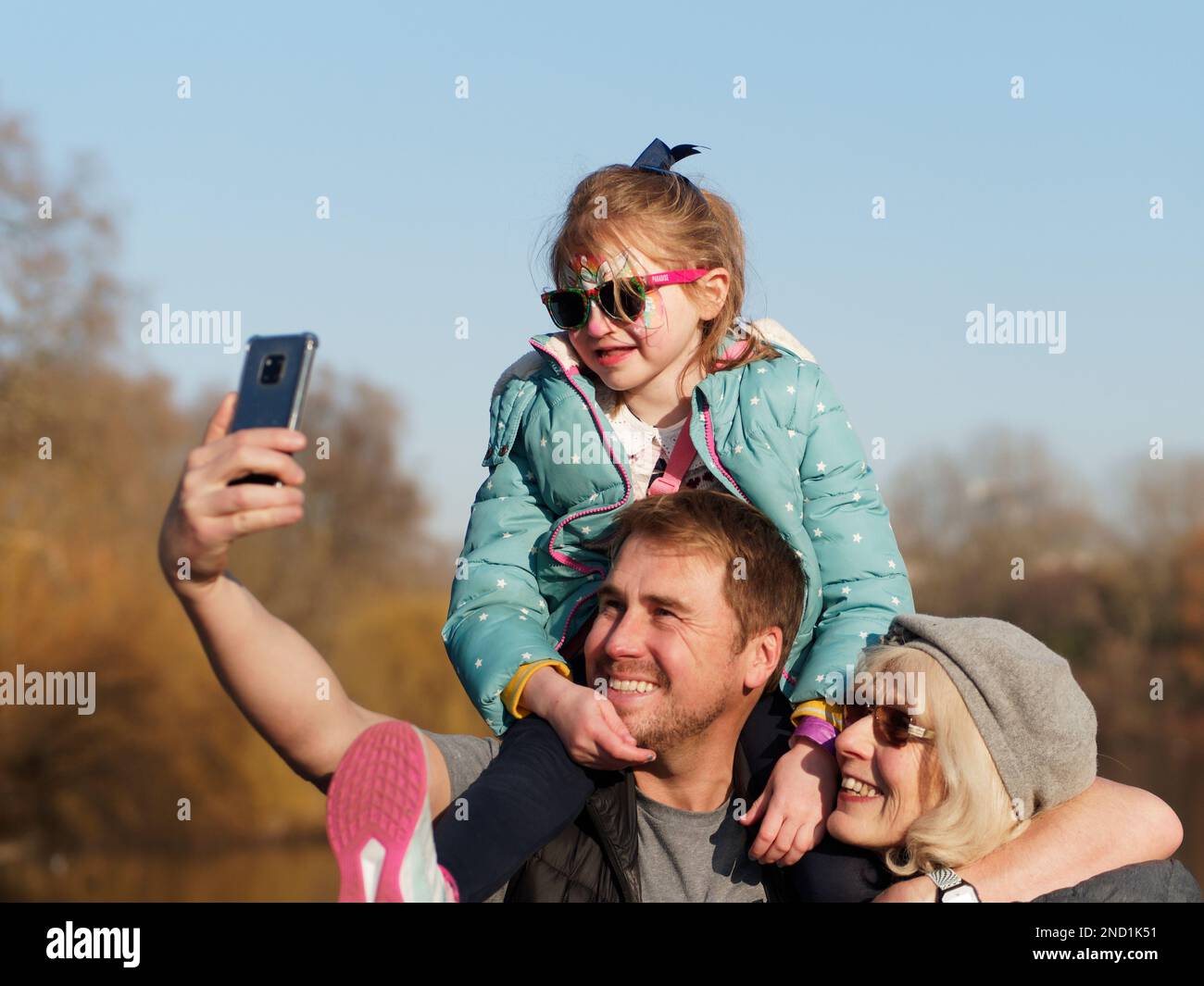 Selfie di famiglia con figlia che indossa occhiali da sole e che si siede sulle spalle dei padri a Londra Foto Stock