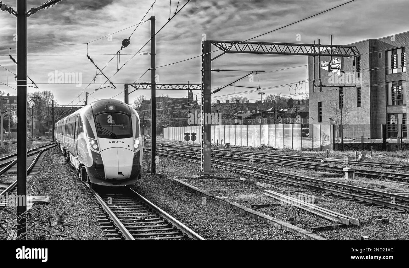 Una locomotiva si avvicina ad una stazione ferroviaria. Le linee elettriche sono sovrastanti e un edificio è un lato. Foto Stock