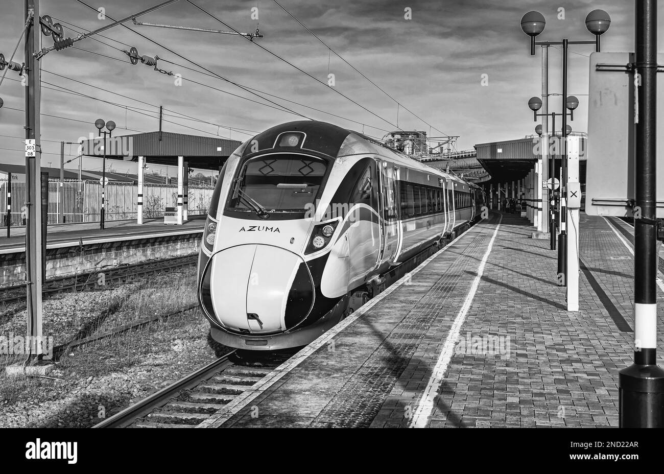 Vista di una stazione ferroviaria con un treno che arriva a un binario. I cavi di alimentazione sono sospesi e sopra c'è un cielo. Foto Stock