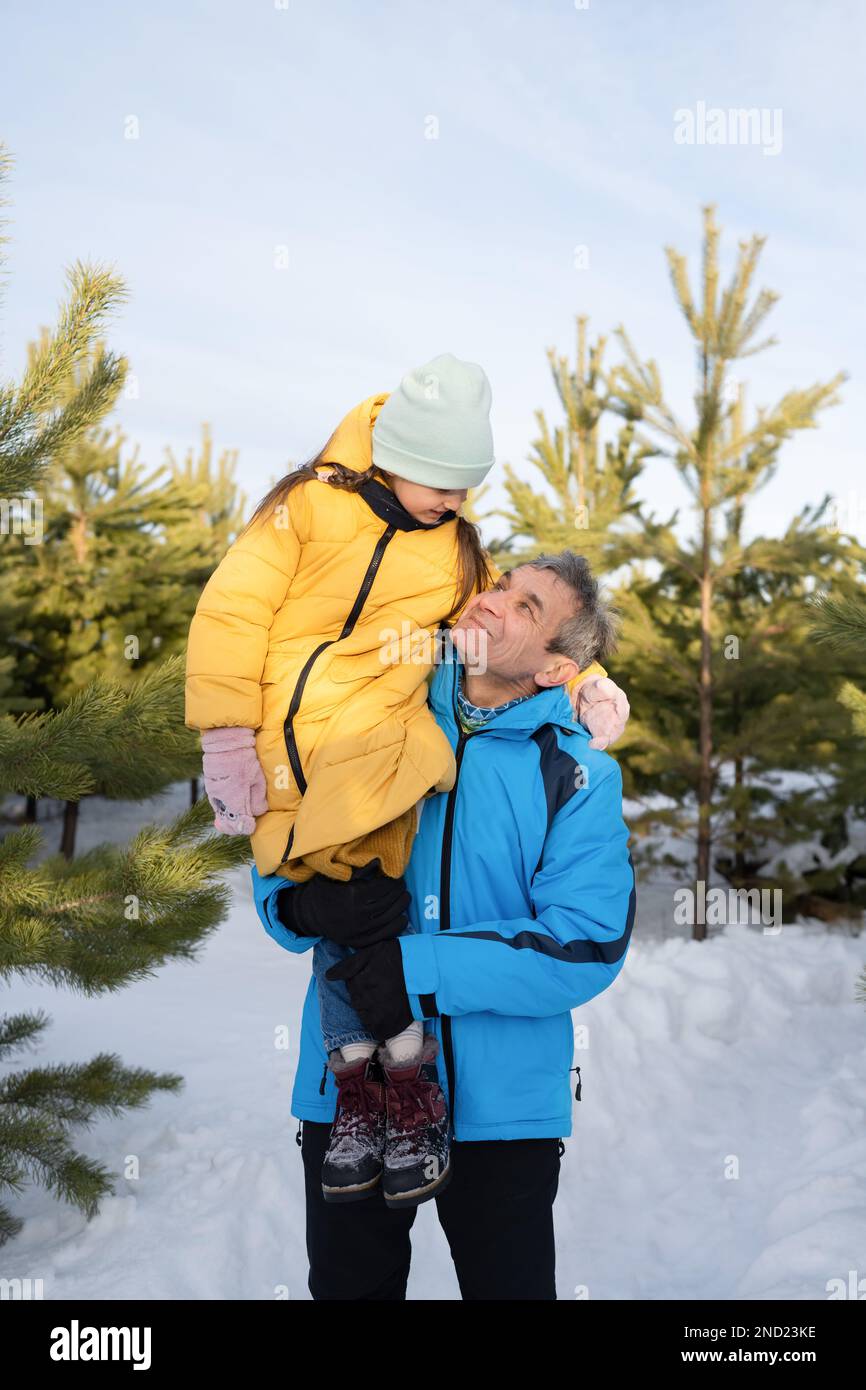 Ragazza prescolare felice che indossa abiti caldi e cappello seduto a spalla del padre durante le vacanze invernali nella foresta innevata Foto Stock