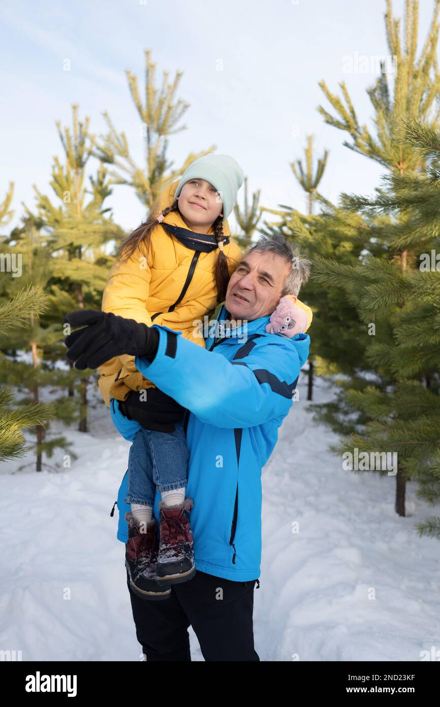 Ragazza prescolare felice che indossa abiti caldi e cappello seduto a spalla del padre durante le vacanze invernali nella foresta innevata Foto Stock