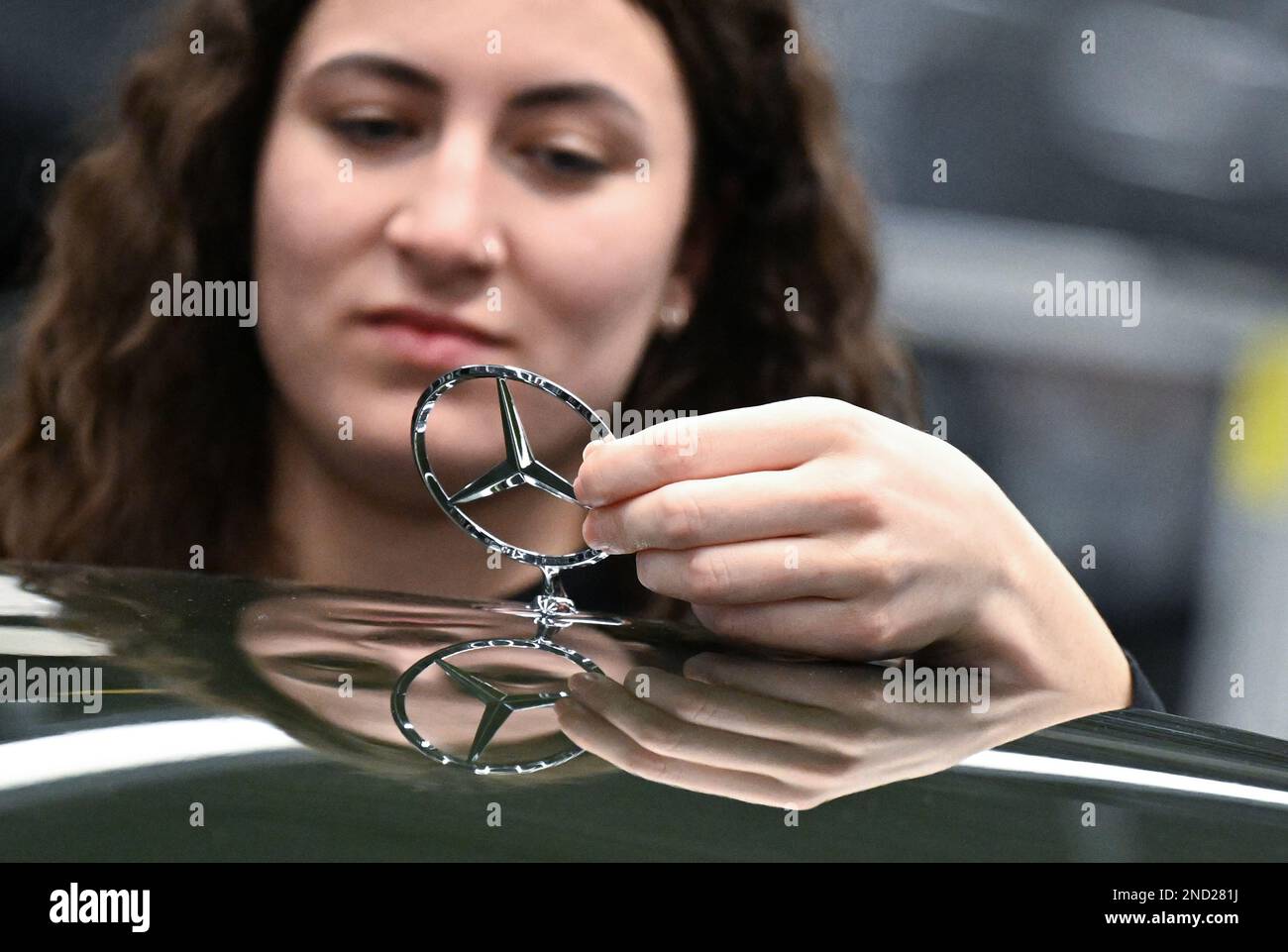 Sindelfingen, Germania. 13th Feb, 2023. Un dipendente del produttore di automobili Mercedes-Benz di Stoccarda lavora su un cofano motore su un emblema Mercedes nella fabbrica 56 dello stabilimento Merecdes-Benz di Sindelfingen, Germania, nella produzione di automobili di lusso e di lusso. Oltre all'EQS, tutte le varianti della Mercedes-Benz S-Class e della Mercedes-Maybach S-Class escono dalla linea di produzione presso lo stabilimento 56. Credit: Bernd Weißbrod/dpa/Alamy Live News Foto Stock