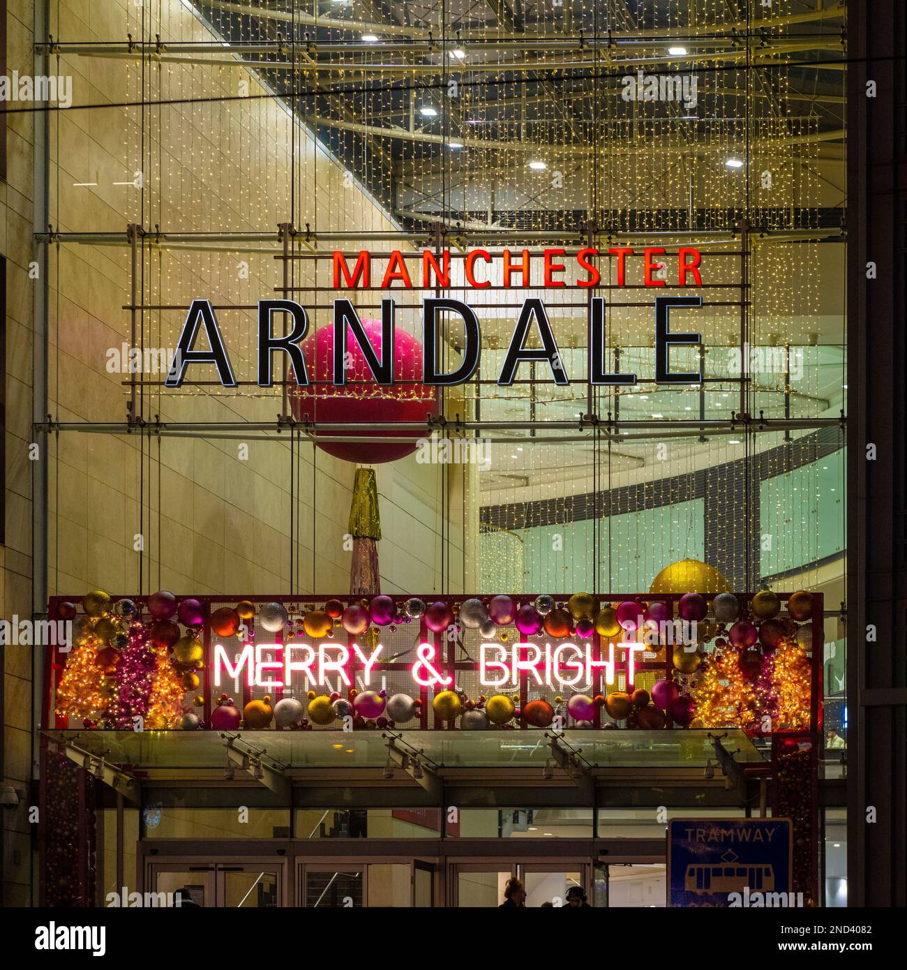 Facciata esterna del centro commerciale Manchester Arndale di notte decorata con baubles di Natale e segno al neon rosa con le parole Merry e Bright Foto Stock