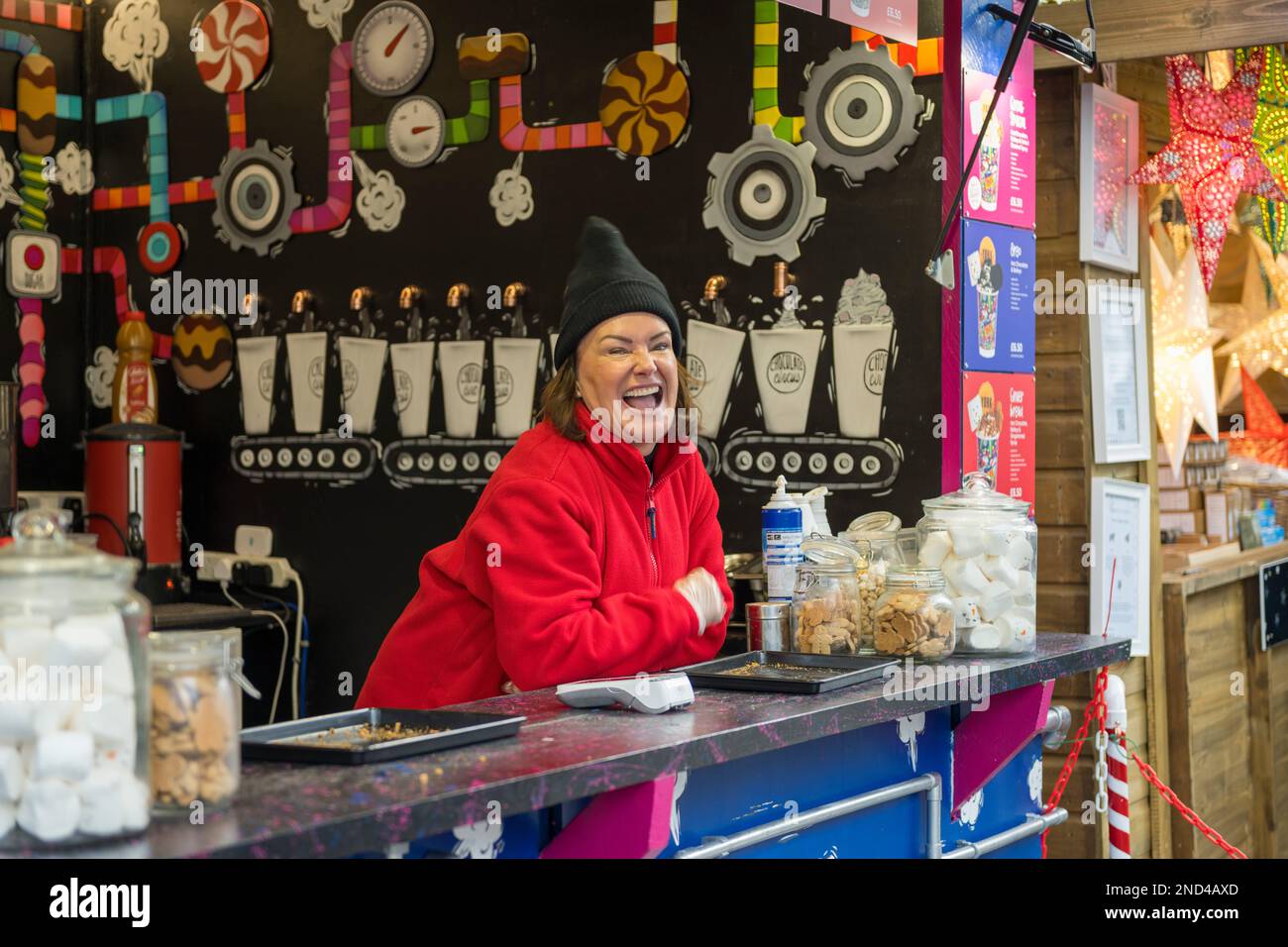 Donna caucasica felice dietro il bancone di una bancarella che vende bevande al cioccolato caldo al mercato di Natale di St Nicholas Fair. York. Foto Stock