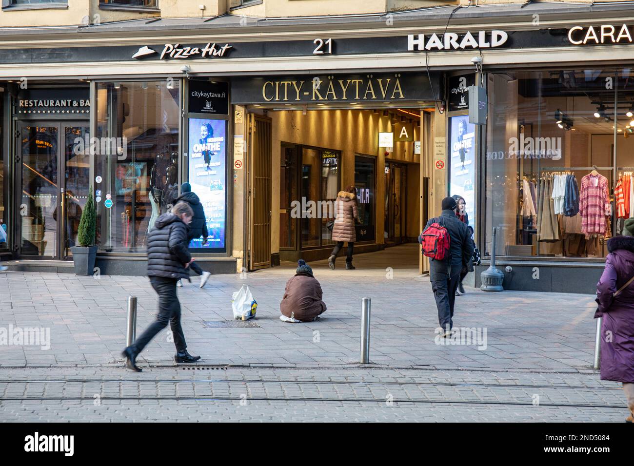 Un anziano che si siede sul marciapiede che prega di fronte a City-käytävä a Helsinki, Finlandia Foto Stock