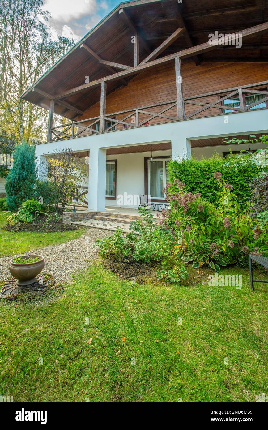 Grande Chalet in stile francese e giardino accanto ad esso con percorso in stile giapponese con giardino di ciottoli e erba verde e cespugli fioriti in autunno (fine della fioritura) Foto Stock