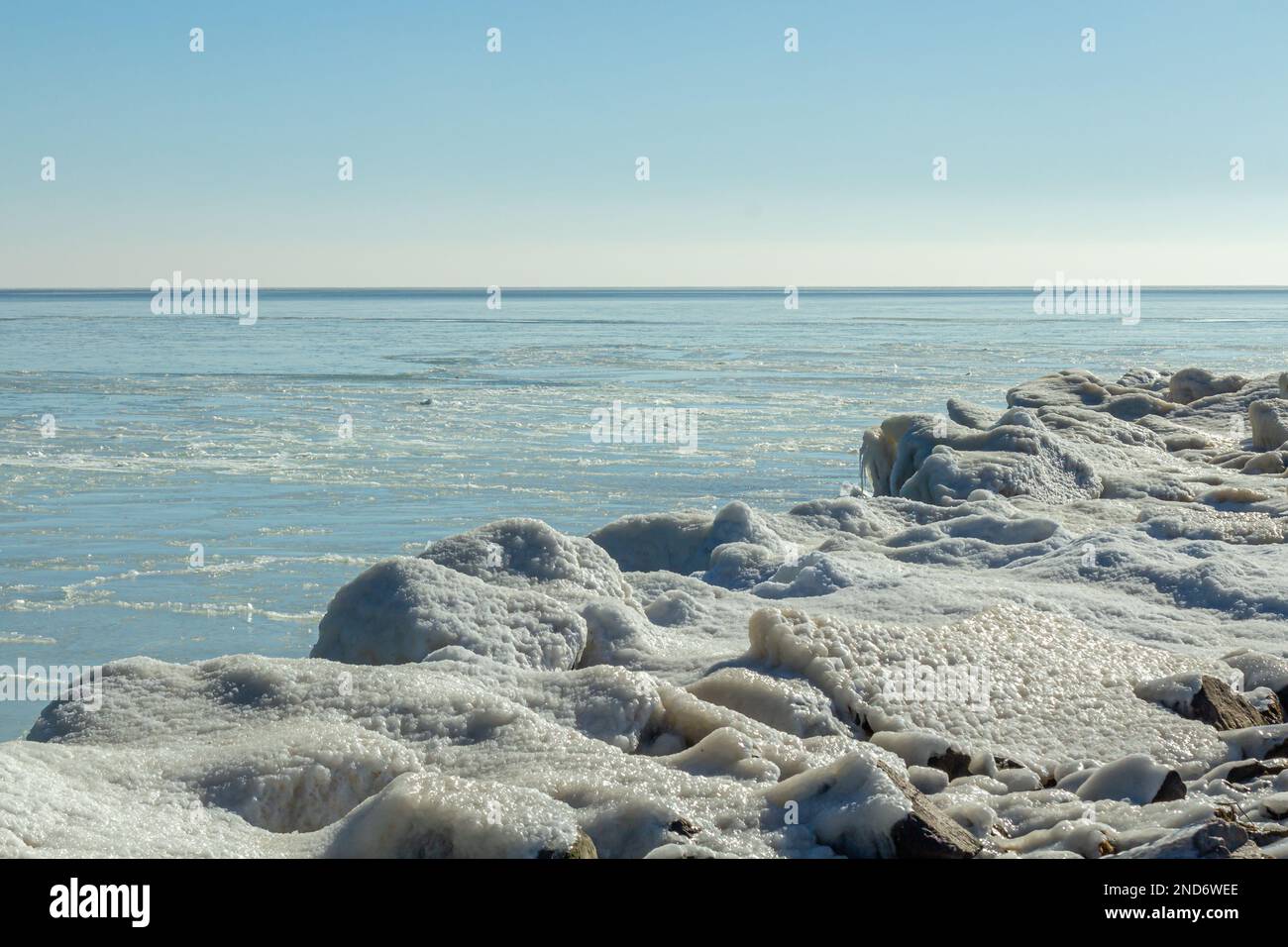 Primo piano della costa ghiacciata, delle onde ghiacciate, delle rocce e del sole che si abbagliano sul ghiaccio. Foto Stock