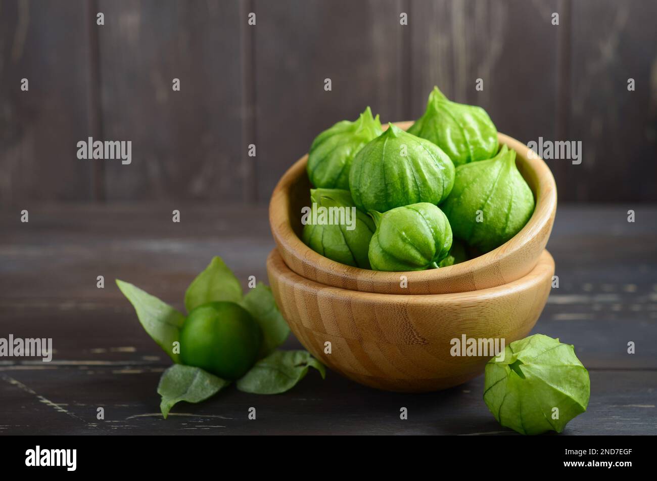 Tomatillos freschi biologici verdi (Physalis philadelphica) con una buccia su un tavolo rustico di legno. Foto Stock