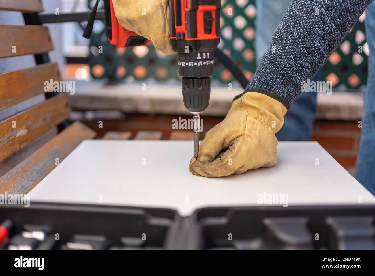 Le mani degli uomini che tengono una vite per avvitarla con una macchina elettrica alimentata a batteria in un legno. Foto Stock