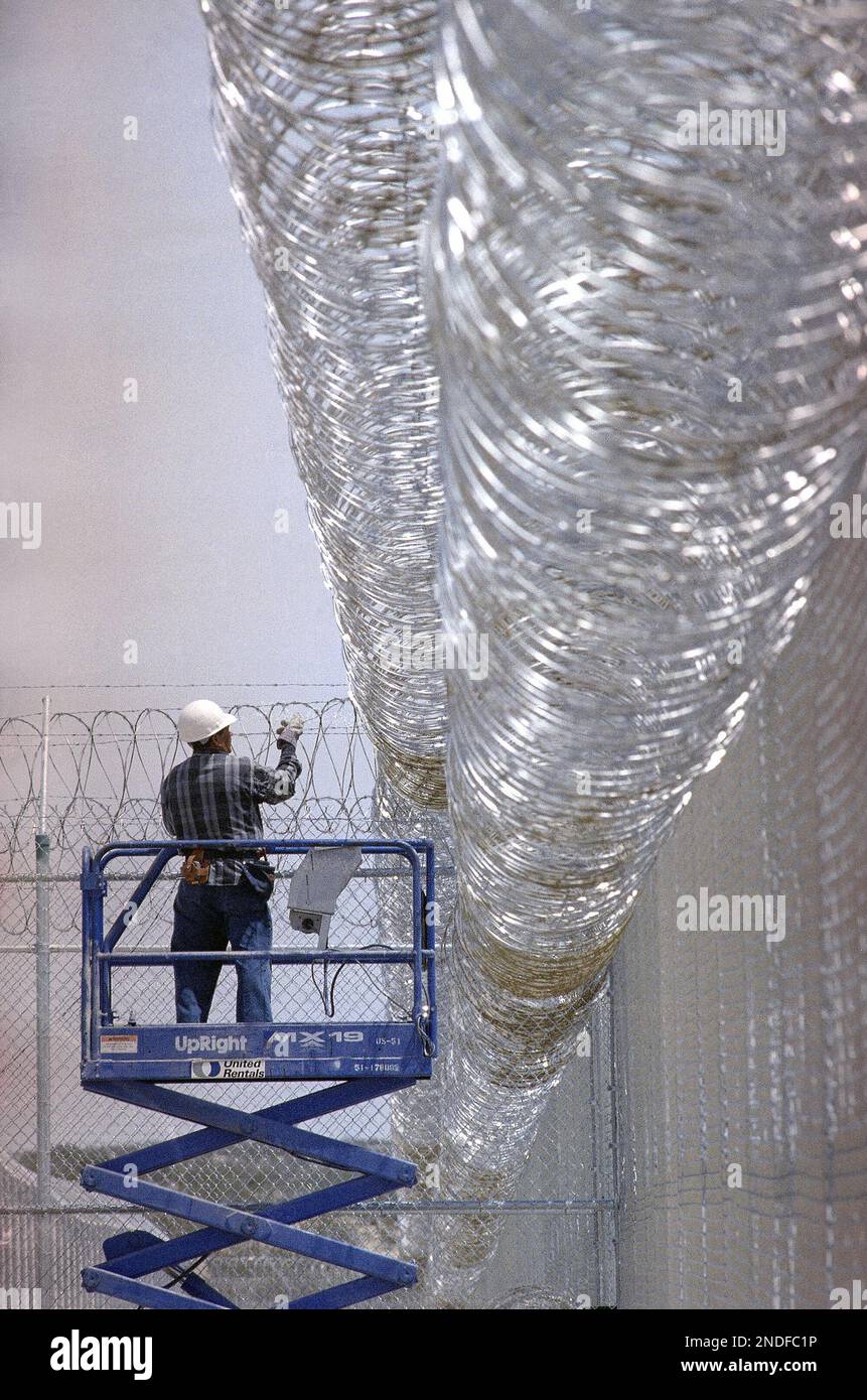 An unidentified worker helps install barbed and razor wire atop a fence ...