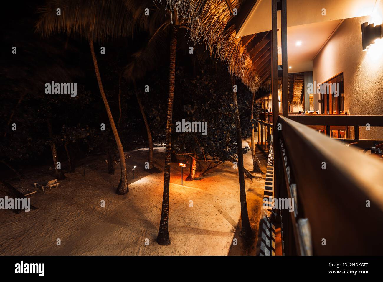 Vista dall'alto in una posizione bassa e lunga dal balcone di un hotel con tetto in paglia all'entrata della proprietà con sabbia bianca, alte palme, e. Foto Stock