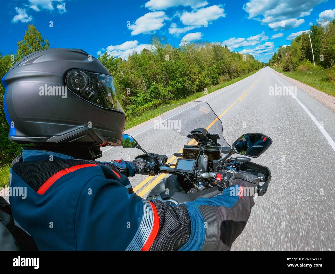 Vista laterale POV motociclista in moto contro il cielo blu, alberi verdi lungo la strada asfaltata. Vista in prima persona. Concentrarsi sul cruscotto di una moto. Foto Stock