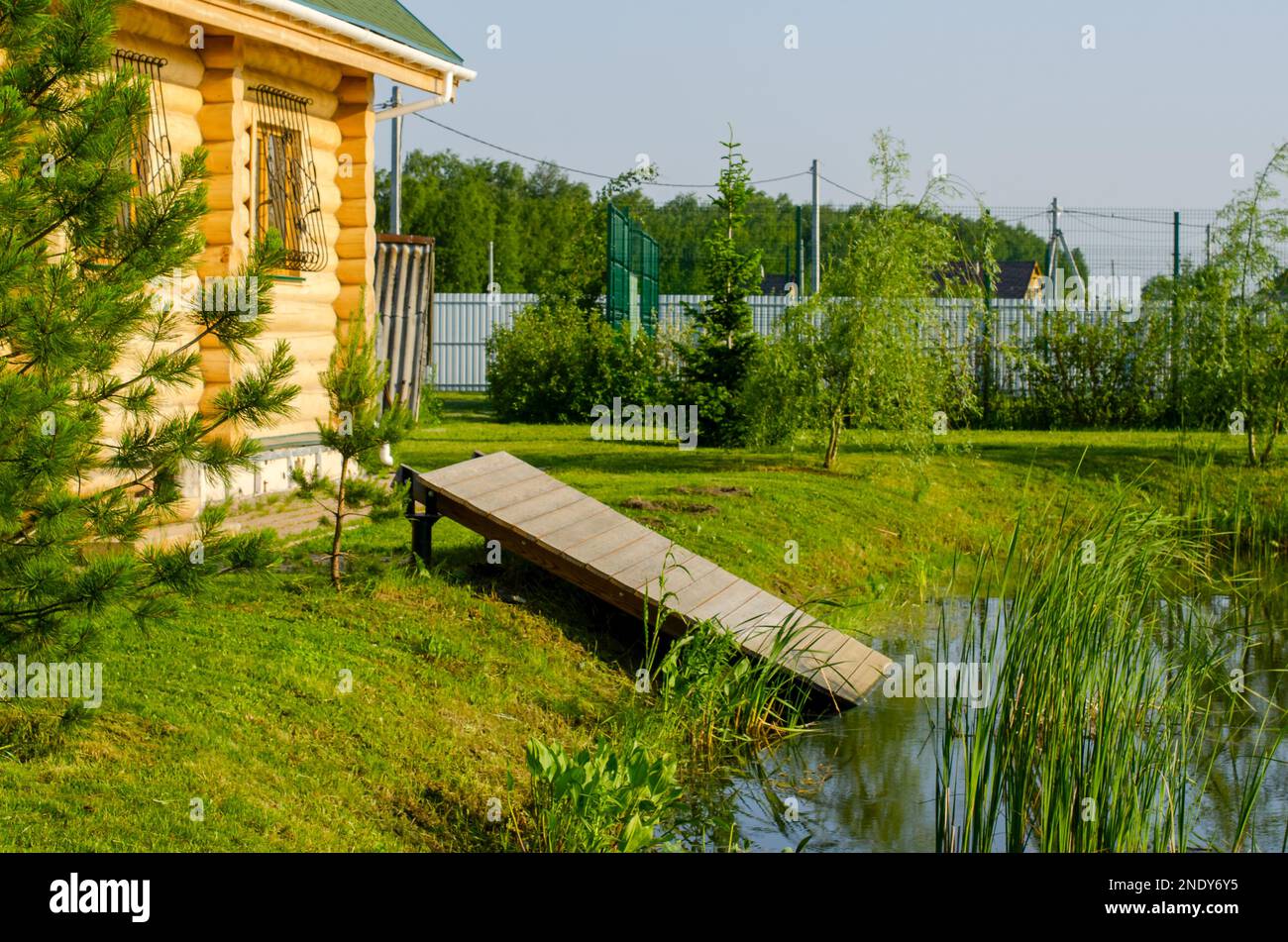 Sauna cottage in legno con discesa nell'acqua del lago su un terreno giardino tra le piante in primavera. Foto Stock