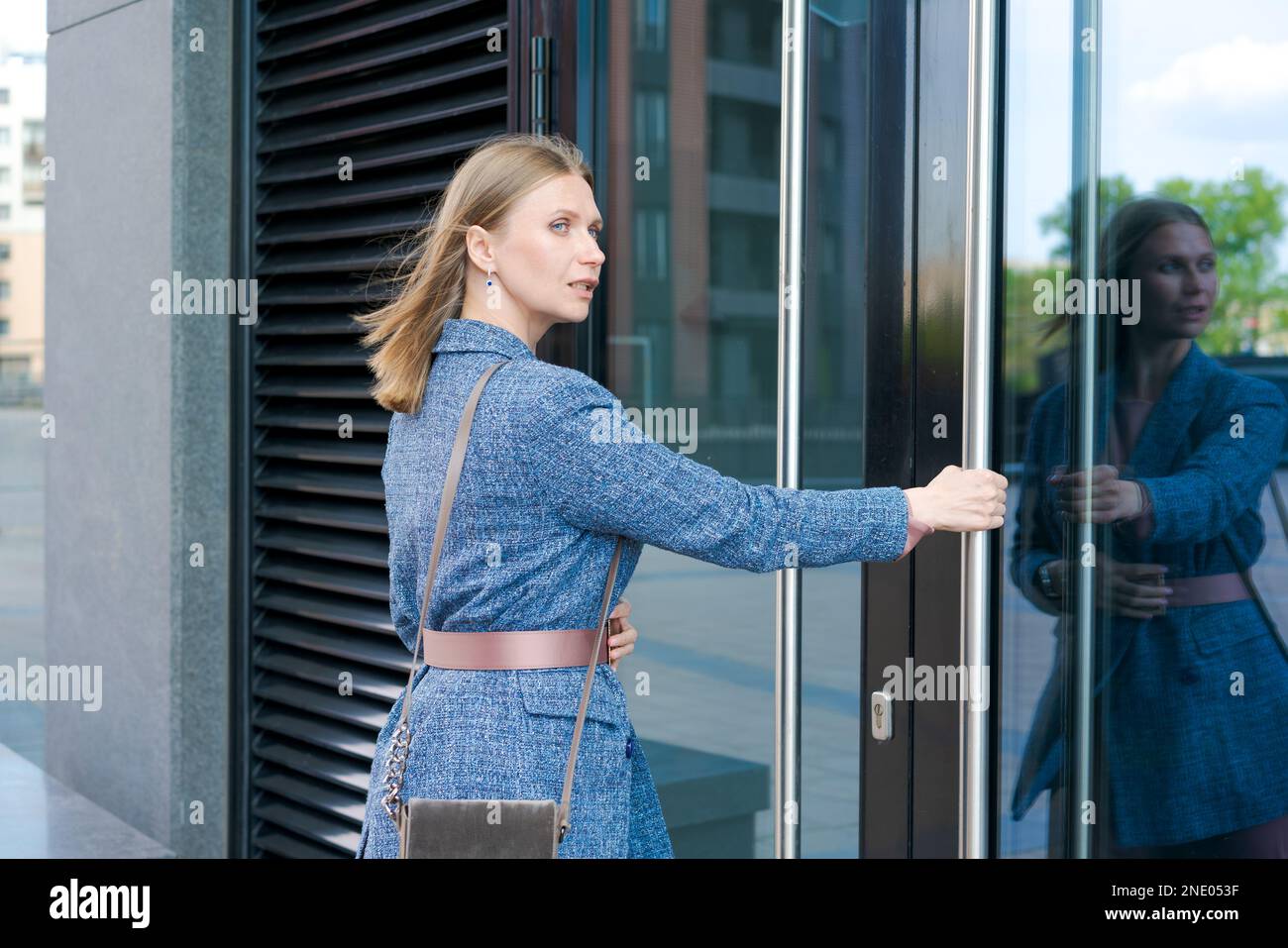Donna felice di affari che mostra i pollici in su mentre levandosi in piedi all'aperto contro lo sfondo dell'edificio dell'ufficio in estate che indossa i vestiti di affari del vincitore e sorridente amichevole riuscito dell'affare, concetto di raccomandazione Foto Stock