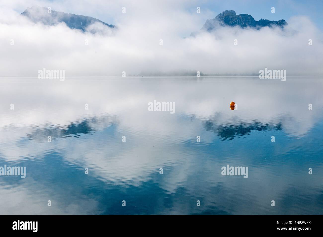 Nella superficie liscia di un lago in montagna riflettono in modo spettacolare le nuvole nei toni blu e grigio. Una boa si trova solo in primo piano i Foto Stock