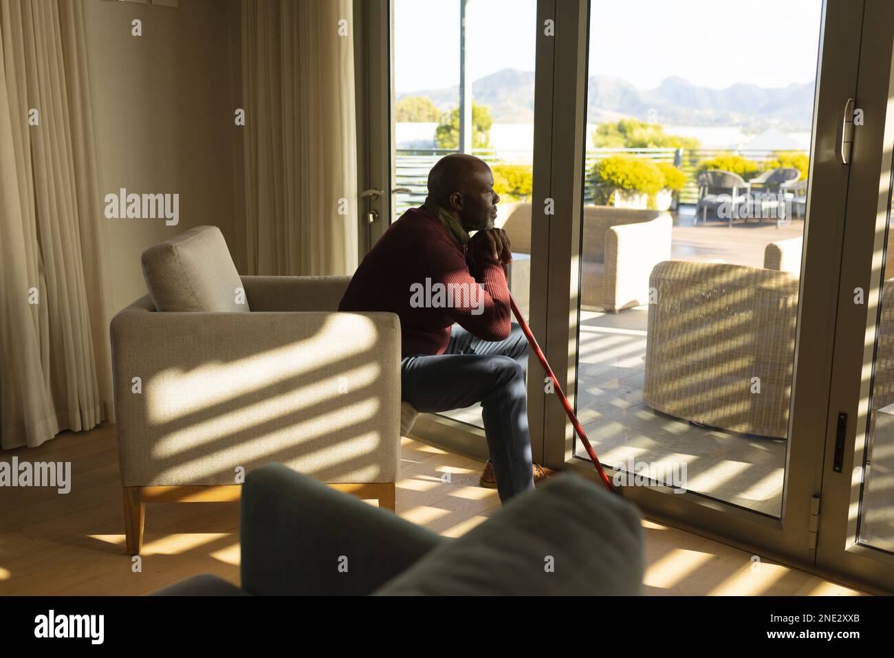 Uomo anziano afro-americano premuroso con bastone che guarda fuori dalla finestra a casa. stile di vita e concetto di vita senior in pensione Foto Stock