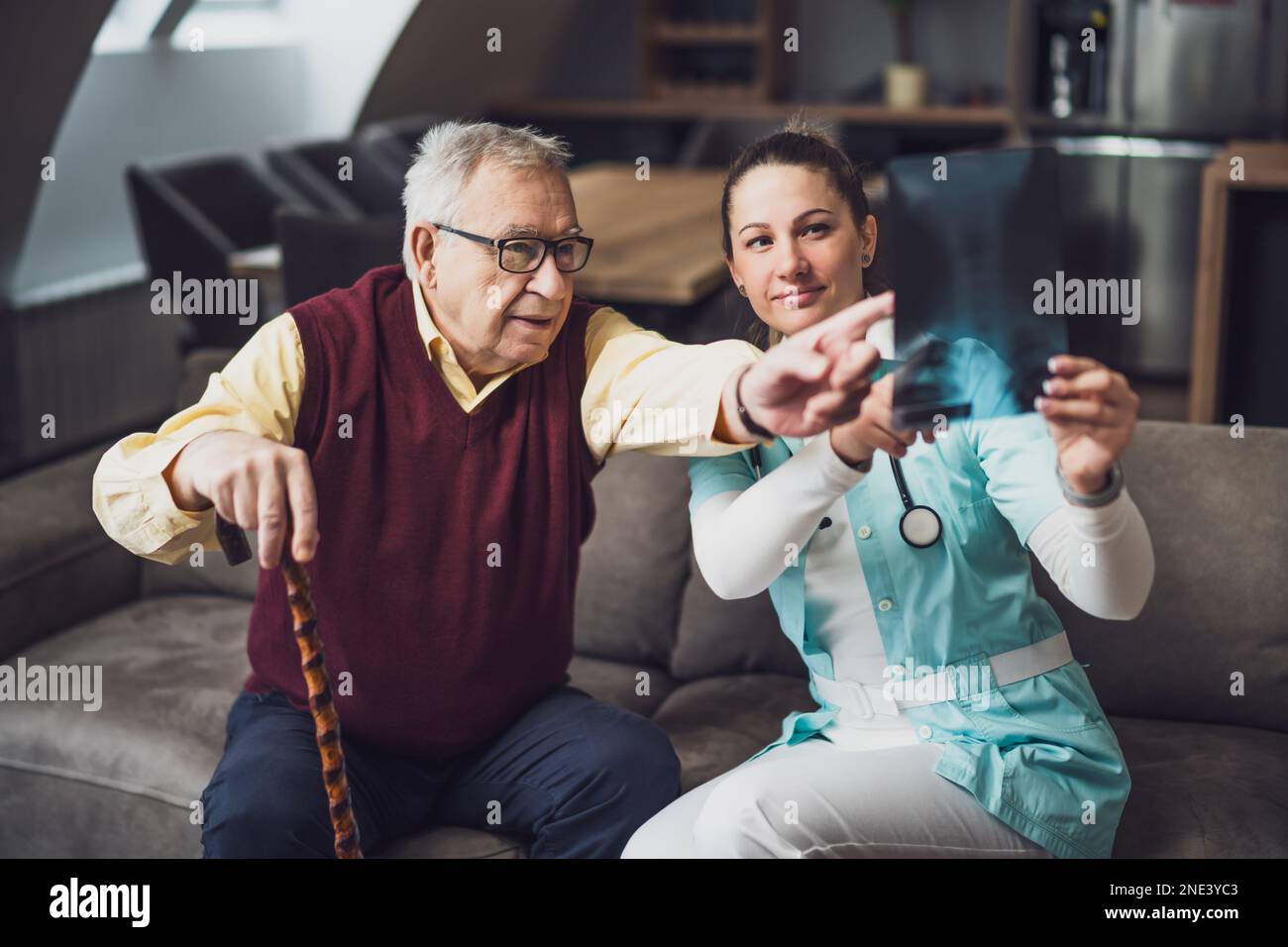 Il medico di casa sta esaminando l'immagine radiografica con il vecchio a casa sua. Assistenza sanitaria professionale per gli anziani. Foto Stock