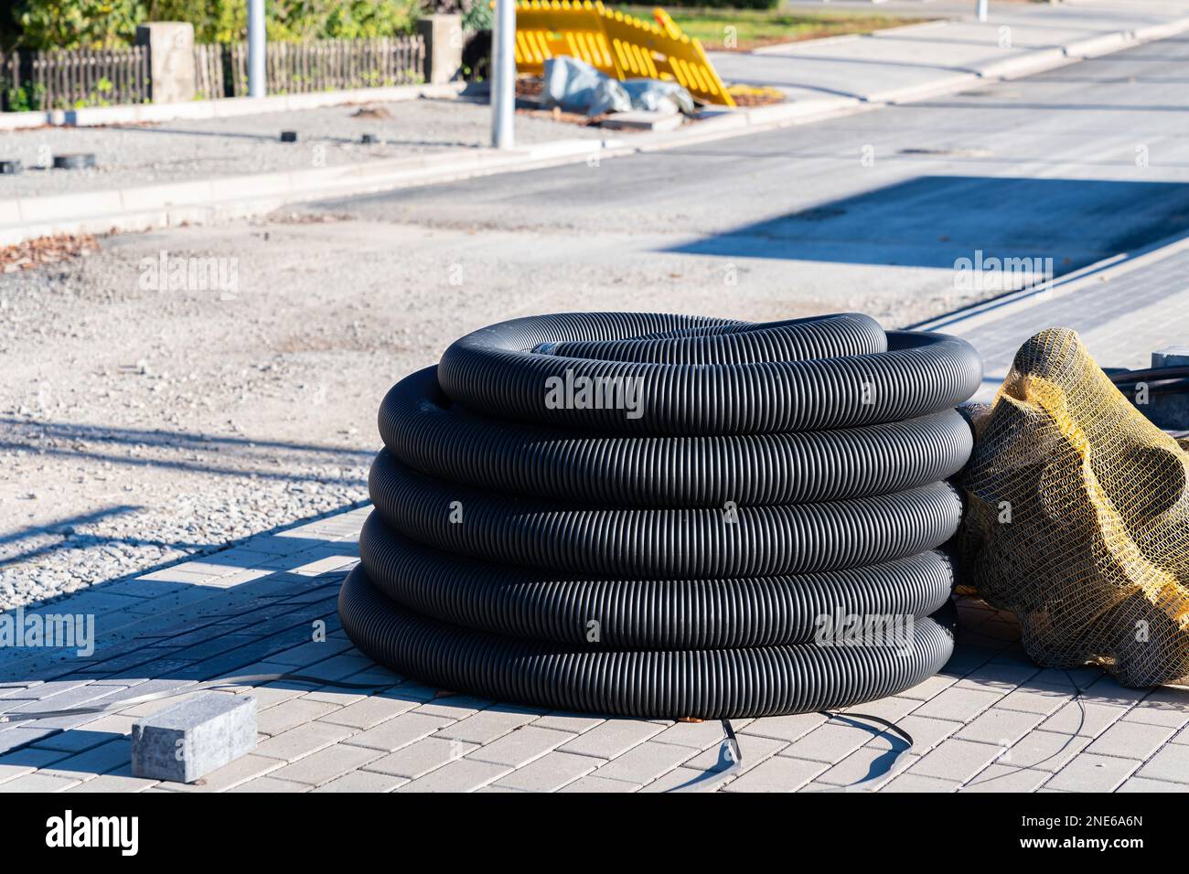 Tubo corrugato nero arrotolato in una bobina in un cantiere. Marciapiede appena asfaltato e costruzione di strade. Foto Stock