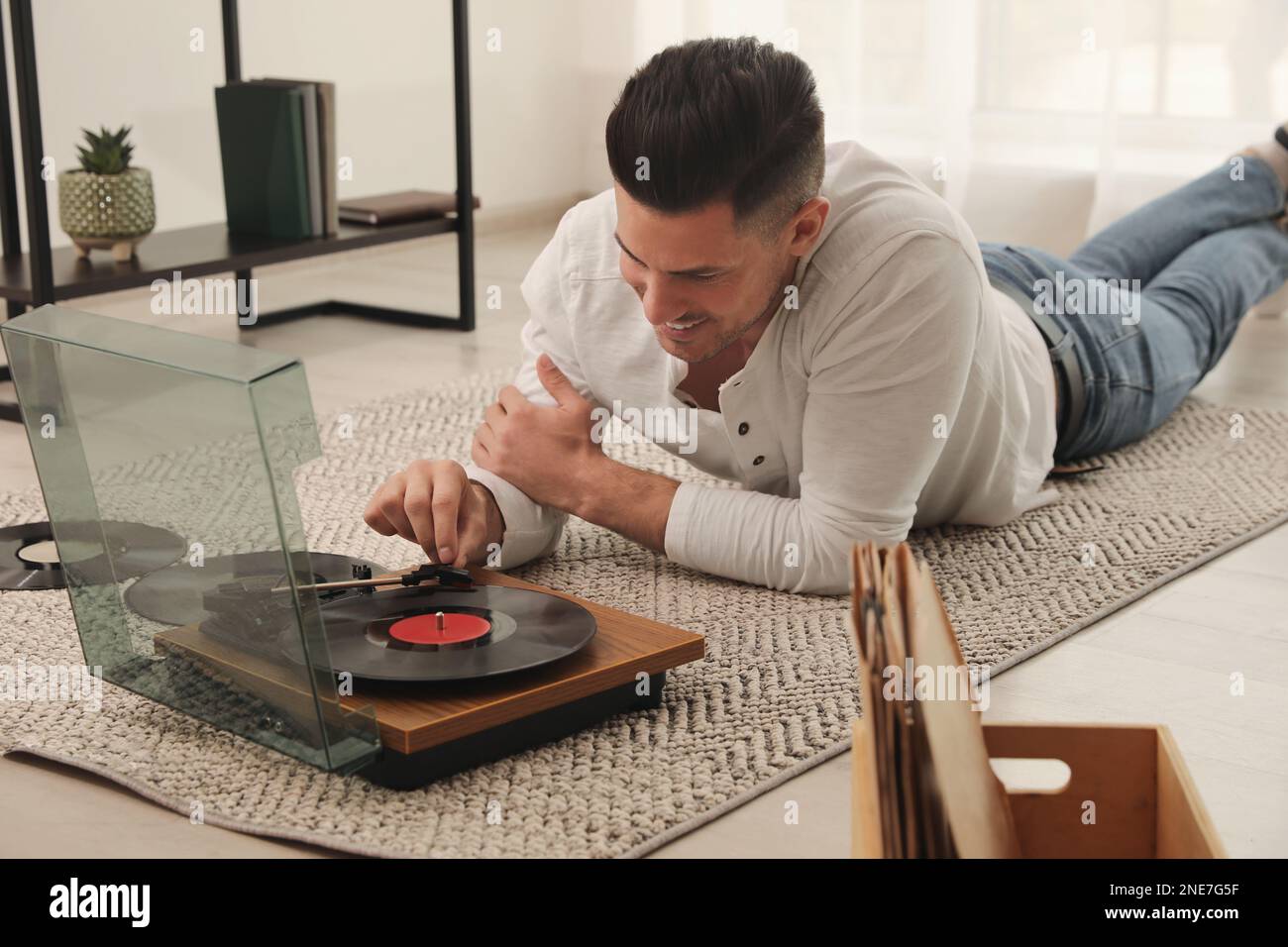 Uomo felice che usa il giradischi mentre si sdraiava sul pavimento a casa Foto Stock