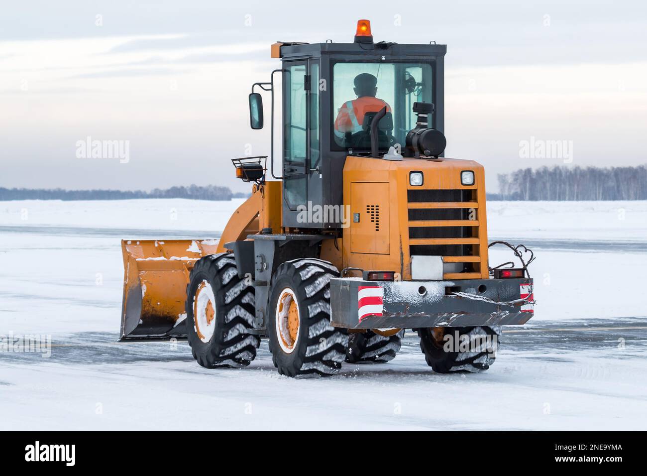 Il trattore gommato giallo pulisce la neve sulla strada Foto Stock