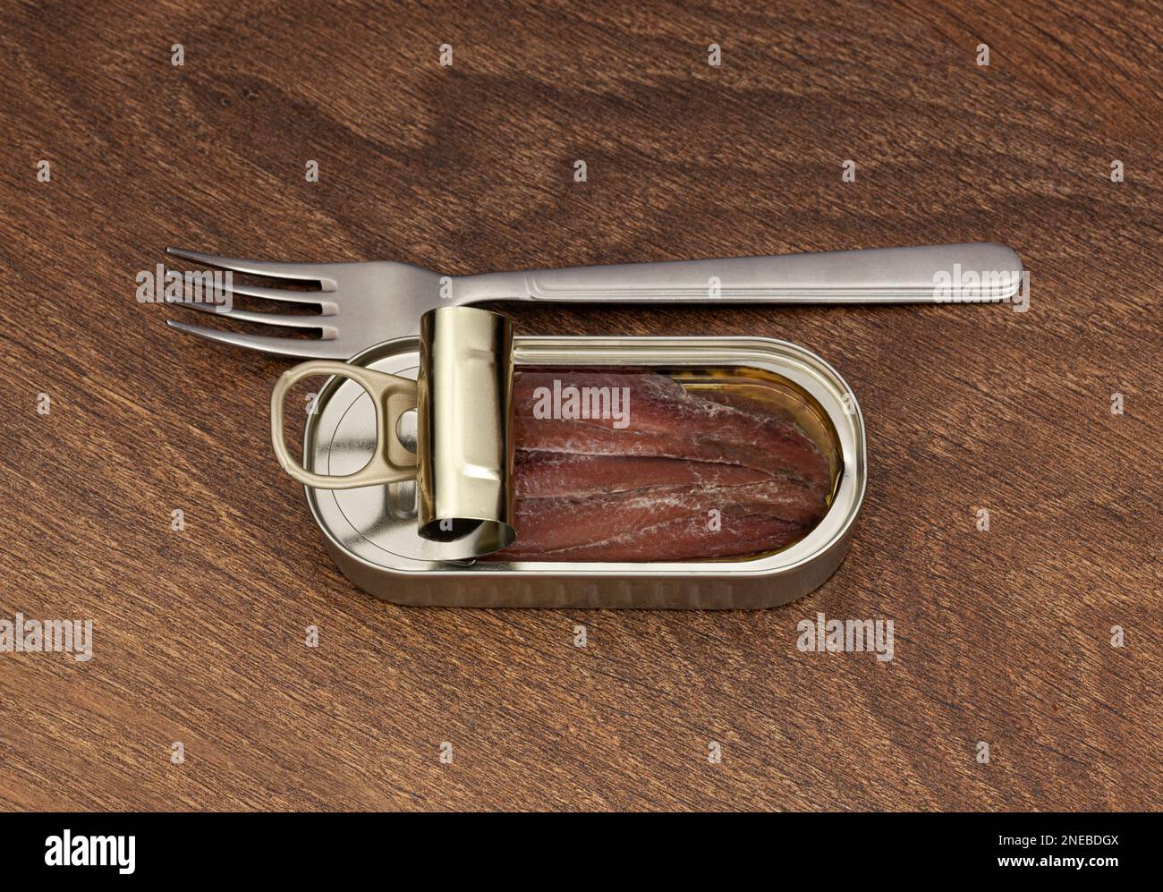 Lattina aperta di filetto di acciuga in olio e forchetta d'argento su fondo in legno. Vista dall'alto Foto Stock