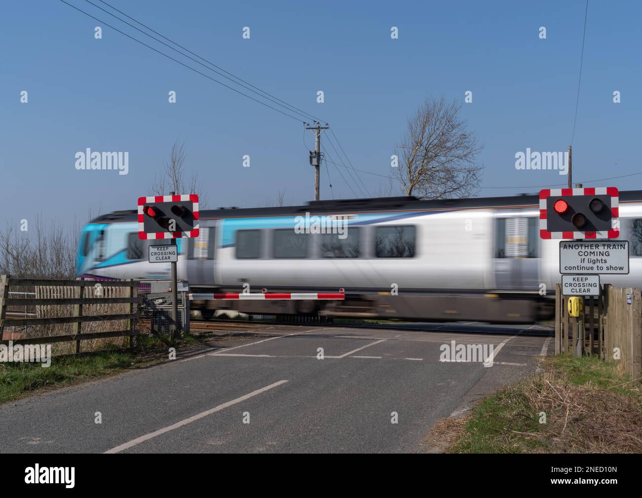 24 marzo 2022 - Un treno in movimento che passa su un passaggio automatico a metà livello della barriera in una giornata limpida con cielo blu. Foto Stock