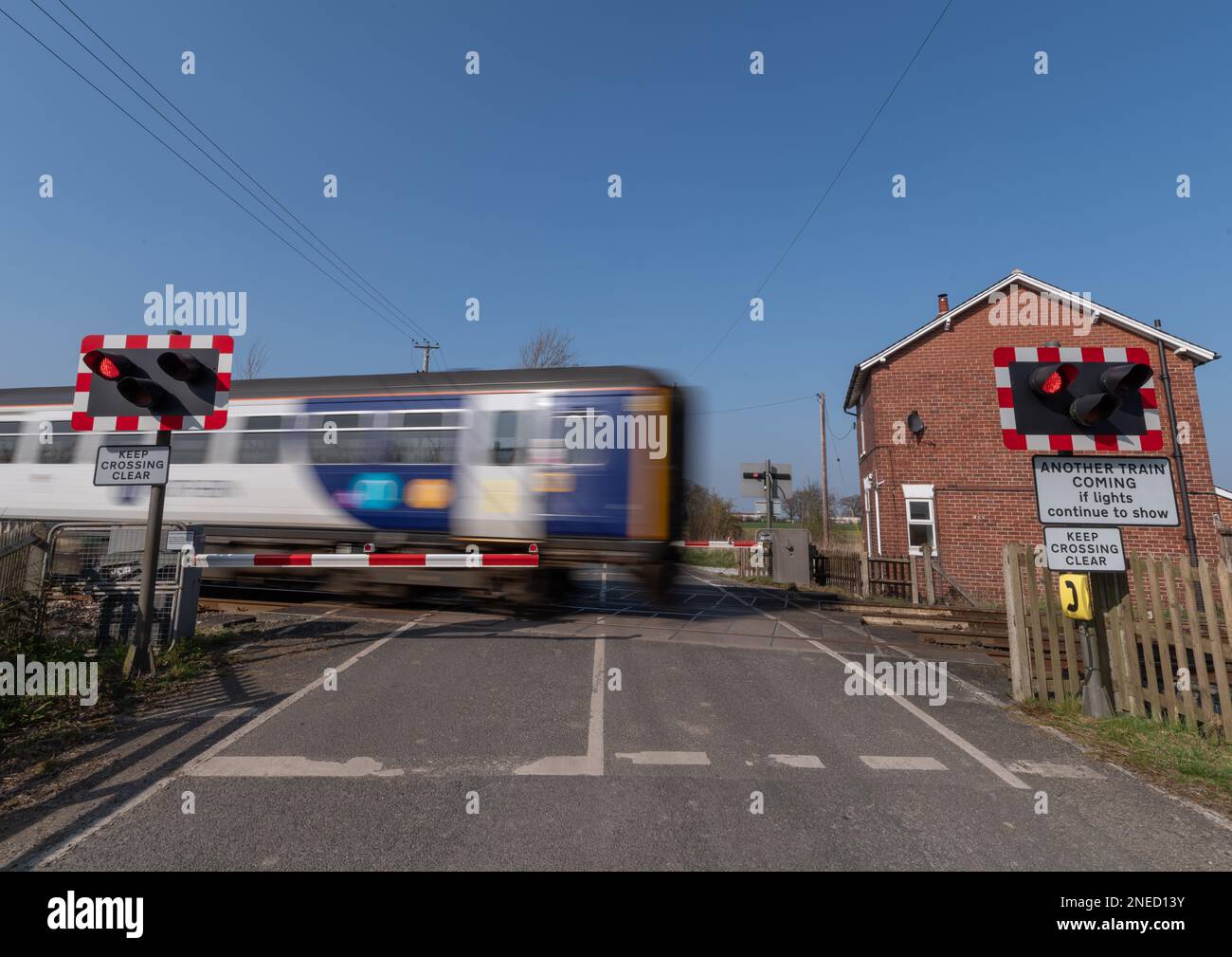 24 marzo 2022 - Un treno in movimento che passa su un passaggio automatico a metà livello della barriera in una giornata limpida con cielo blu. Foto Stock