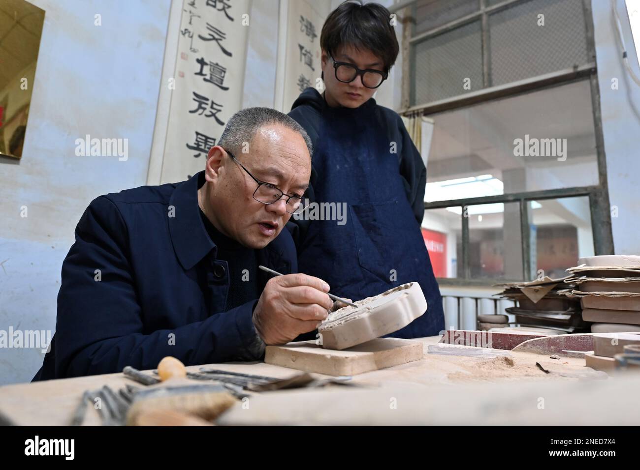 (230216) -- YUNCHENG, 16 febbraio 2023 (Xinhua) -- LIN Tao (L), un erede rappresentativo del mestiere di fabbricazione della pietra di increspatura di Chengni a livello provinciale, guida suo figlio Lin Xiaolin sui dettagli dell'intaglio sulla pietra di increspatura di Chengni nel villaggio di Guangcun della contea di Xinjiang a Yuncheng, provincia di Shanxi della Cina settentrionale, 14 febbraio 2023. Chengni inkstone, uno dei "quattro famosi inkstone" in Cina, è noto per la sua consistenza fine che può ridurre il danno fatto al pennello. A causa di varie ragioni, l'artigianato di Chengni fu una volta perso e successivamente riportato da Lin Yongmao and Foto Stock